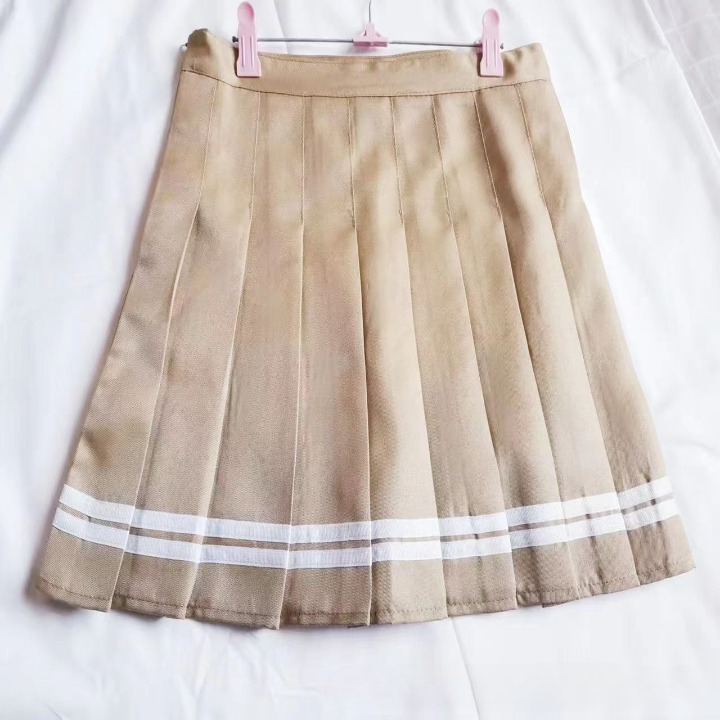 A close-up of a beige pleated skirt with white stripe accents, hung on a soft white background. The image showcases the design and structure of the skirt, ideal for femboy clothing enthusiasts looking for a versatile addition to their femboy outfits or femboy fashion collections.