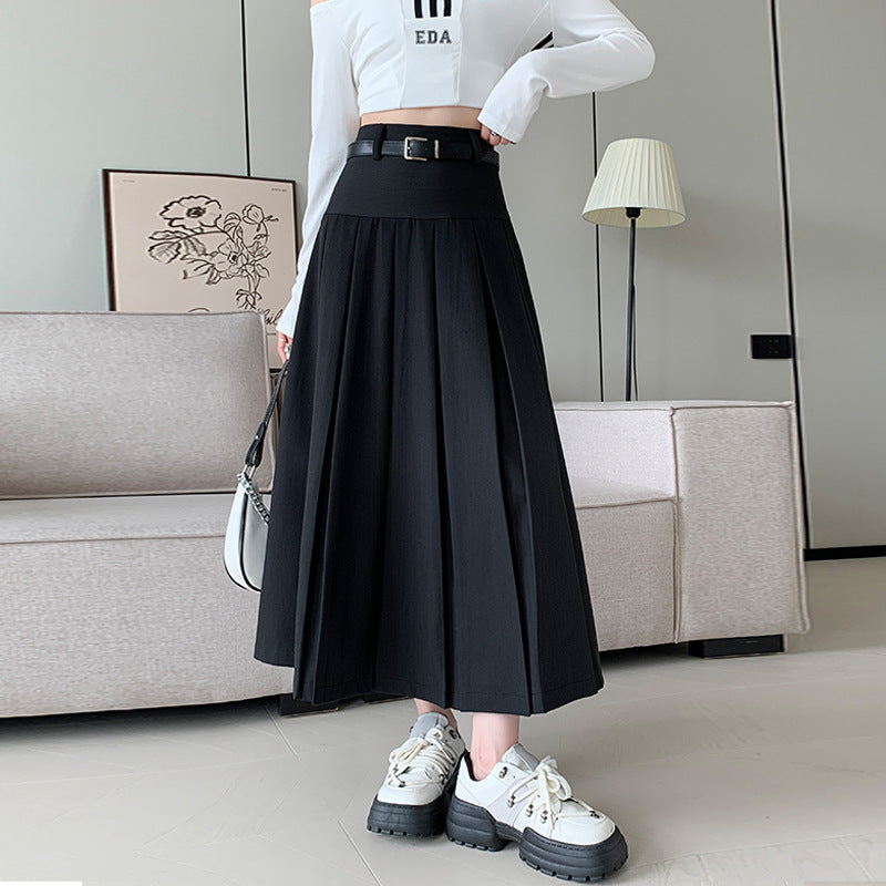 Medium shot of a model wearing a black midi pleated skirt, styled with a high waist and black belt, representing femboy outfits, photographed in a modern, light-filled room.