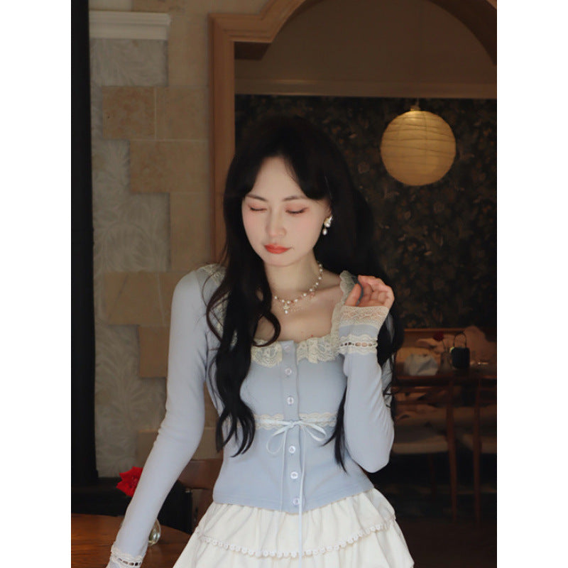 Front view of a blue Lace Cardigan Top with intricate lace trim and a ribbon tie, paired with a cream layered skirt. Captured indoors in a cosy, warm setting, highlighting femboy clothes and femboy style.