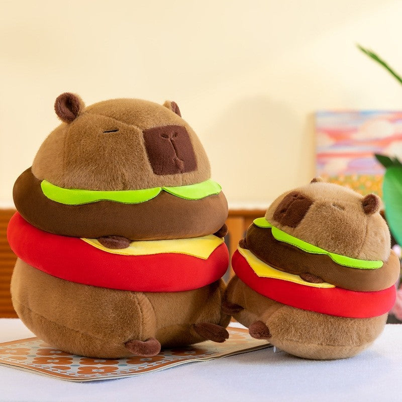 Side profile view of two Capybara Burger Plush toys in different sizes, highlighting the rounded shape, embroidered facial details, and layered hamburger design.