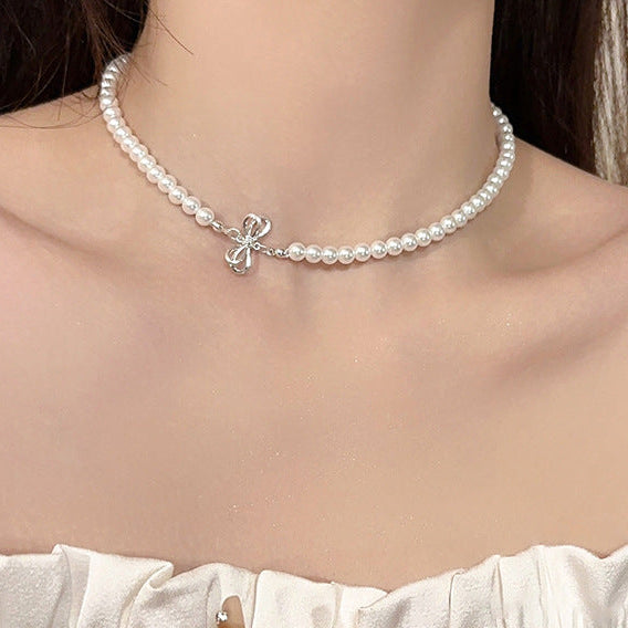 Elegant pearl necklace with a silver bow pendant, styled on a model wearing an off-shoulder white outfit, highlighting femboy fashion.