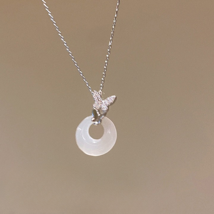Stylish silver necklace featuring a butterfly charm and clear crystal ring, presented against a soft beige background for a chic femboy look.