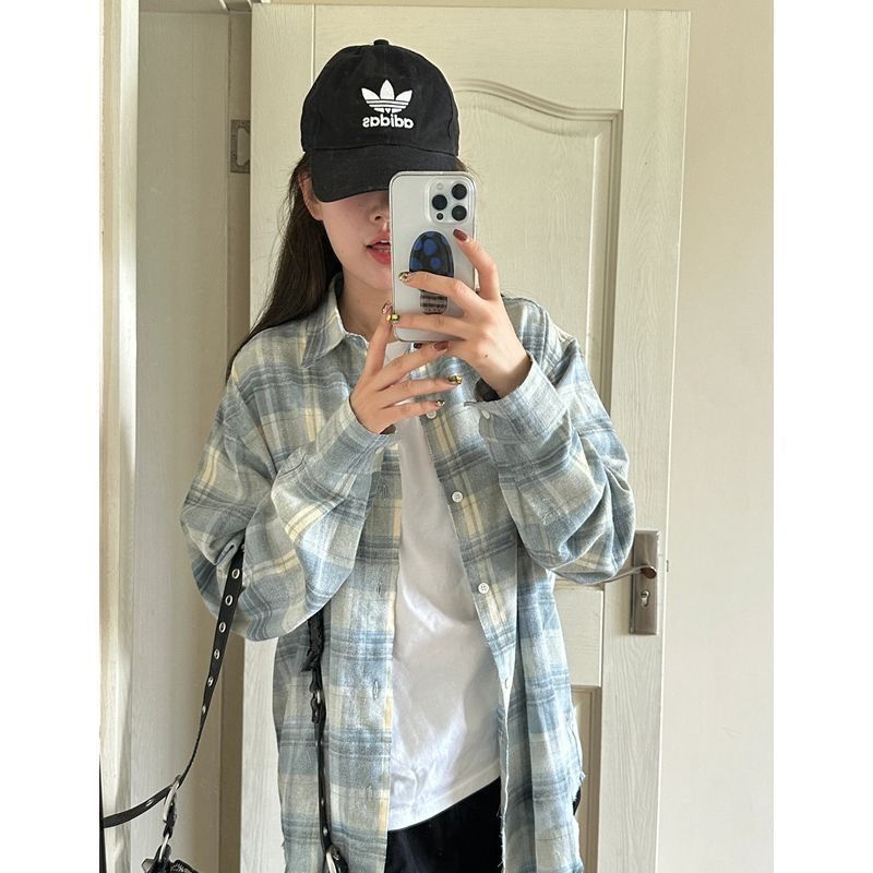Mirror selfie of a person wearing a blue plaid button-up shirt paired with a black cap and white t-shirt, showcasing a casual femboy outfit. The image captures the relaxed style of femboy clothing.