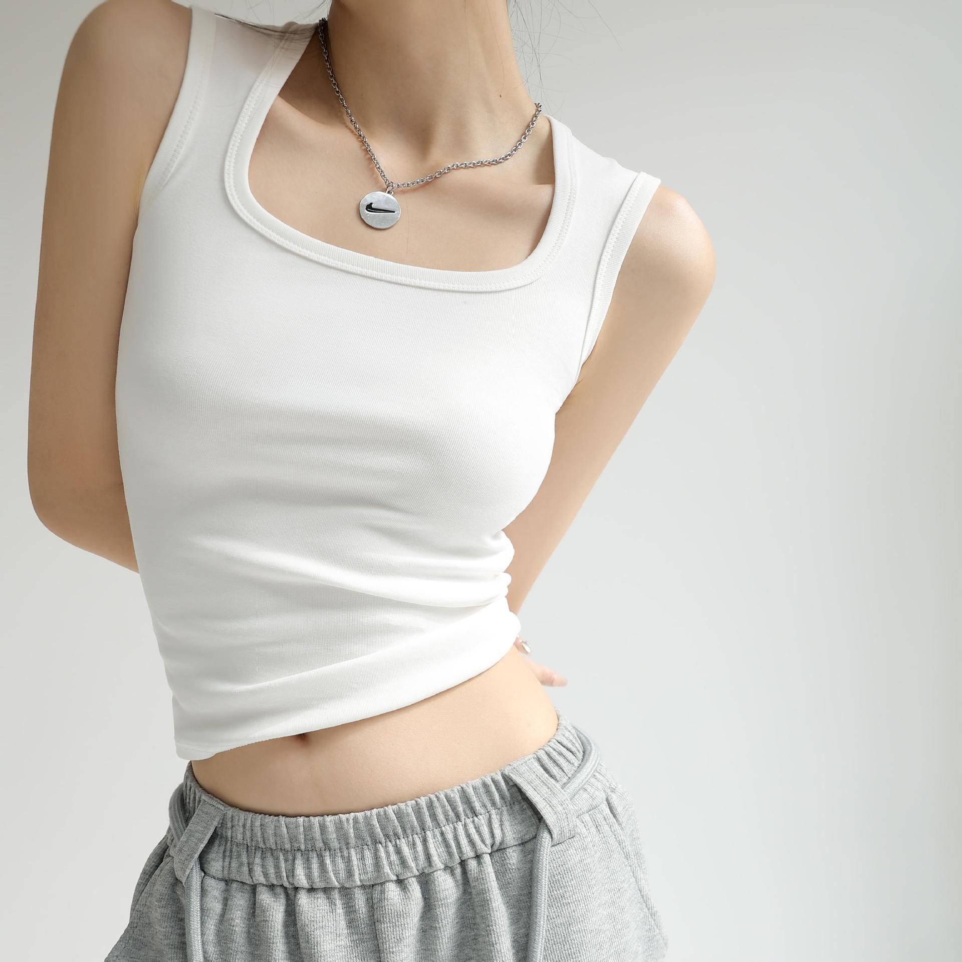 White femboy cotton tank top featuring a smooth fitted silhouette and sleeveless scoop neckline, worn by an androgynous model styled with grey joggers, minimal neutral studio background.