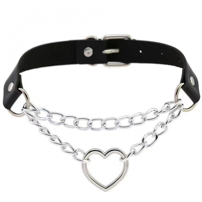 Black leather gothic femboy choker with silver heart ring centerpiece and double chain detailing, photographed on a clean white background, styled as edgy femboy fashion accessory.