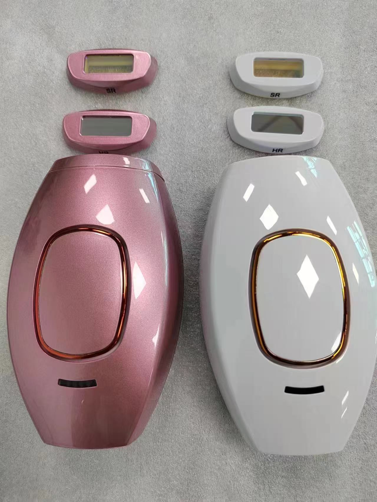 Pink and white femboy IPL hair removal devices displayed side by side with detachable treatment heads above each unit, showcasing color options and sleek ergonomic design on a neutral grey surface