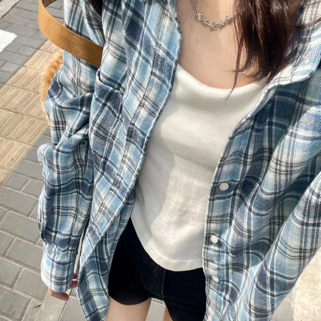 Overhead view of a person wearing a blue plaid button-up shirt over a white tank top, styled with black shorts and sneakers, walking on a city street. The shot highlights the versatility of femboy outfits.