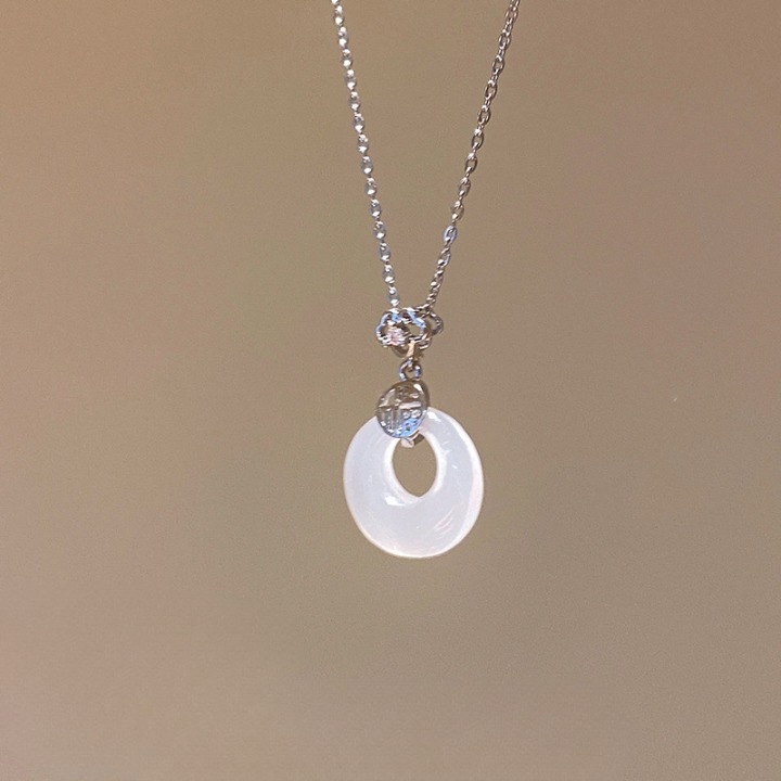 Close-up of a delicate pendant necklace with a circular charm on a minimalist background, ideal for femboy fashion outfits.