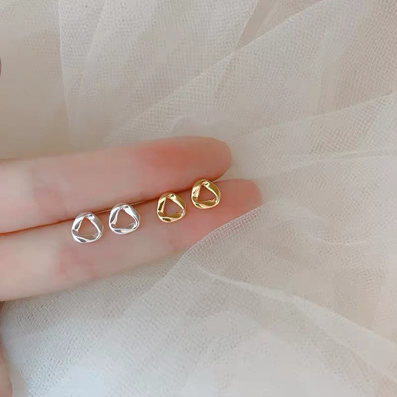 Gold and silver mobius strip earrings placed on a delicate white fabric, embodying femboy style and modern chic.