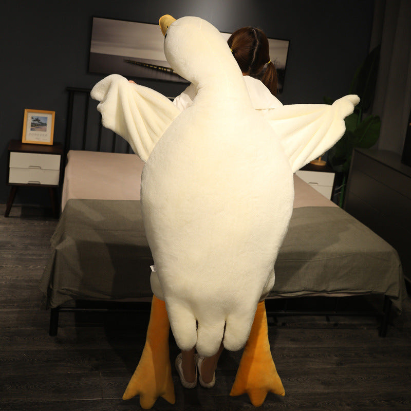 Full-length goose plush body pillow shown from the back, featuring soft white fabric, oversized wings, and extended legs, displayed in a bedroom setting to demonstrate its large cuddle size.