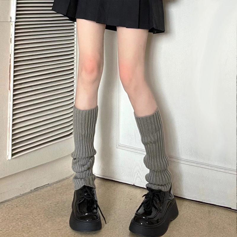 Gray knitted leg warmers layered with a black skirt and platform shoes, relaxed cozy femboy clothing style with a casual streetwear vibe.