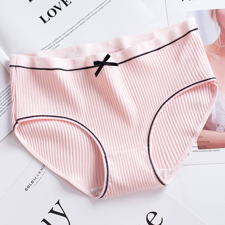 overhead shot of a soft pastel pink ribbed brief with black piping and a tiny bow accent, arranged on a white table with cotton accents, highlighting pastel femboy clothes.