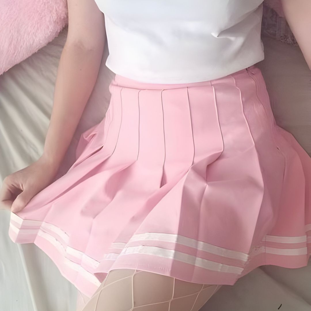 Soft pastel pink pleated femboy skirt worn with a white top, close-up lifestyle shot highlighting the flowy fabric, clean pleats, and gentle feminine silhouette for a cute femboy outfit aesthetic.