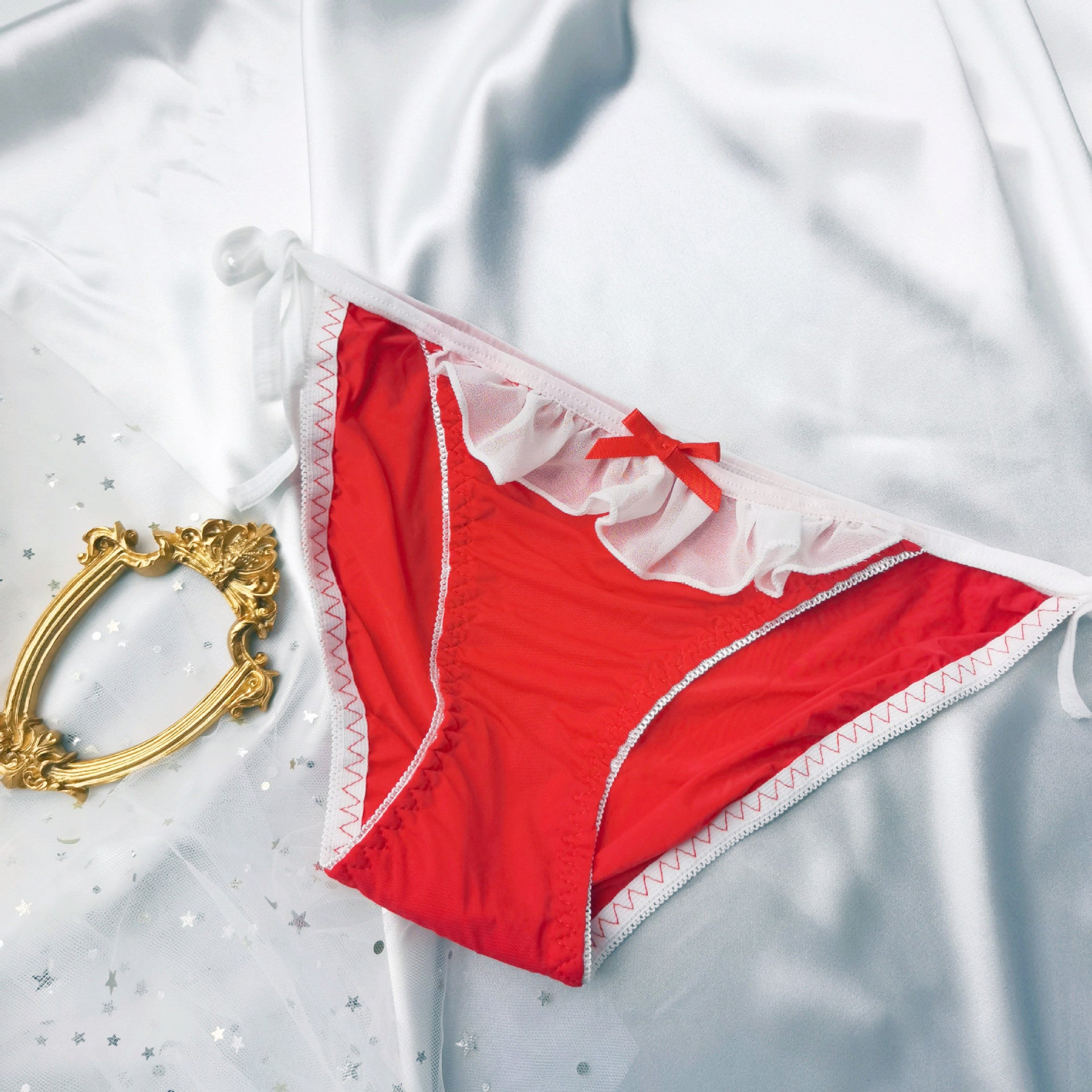 Flat lay top view of red Lolita maid lace-up panties with white frill trim and red bow on satin background – bold sexy femboy panties aesthetic