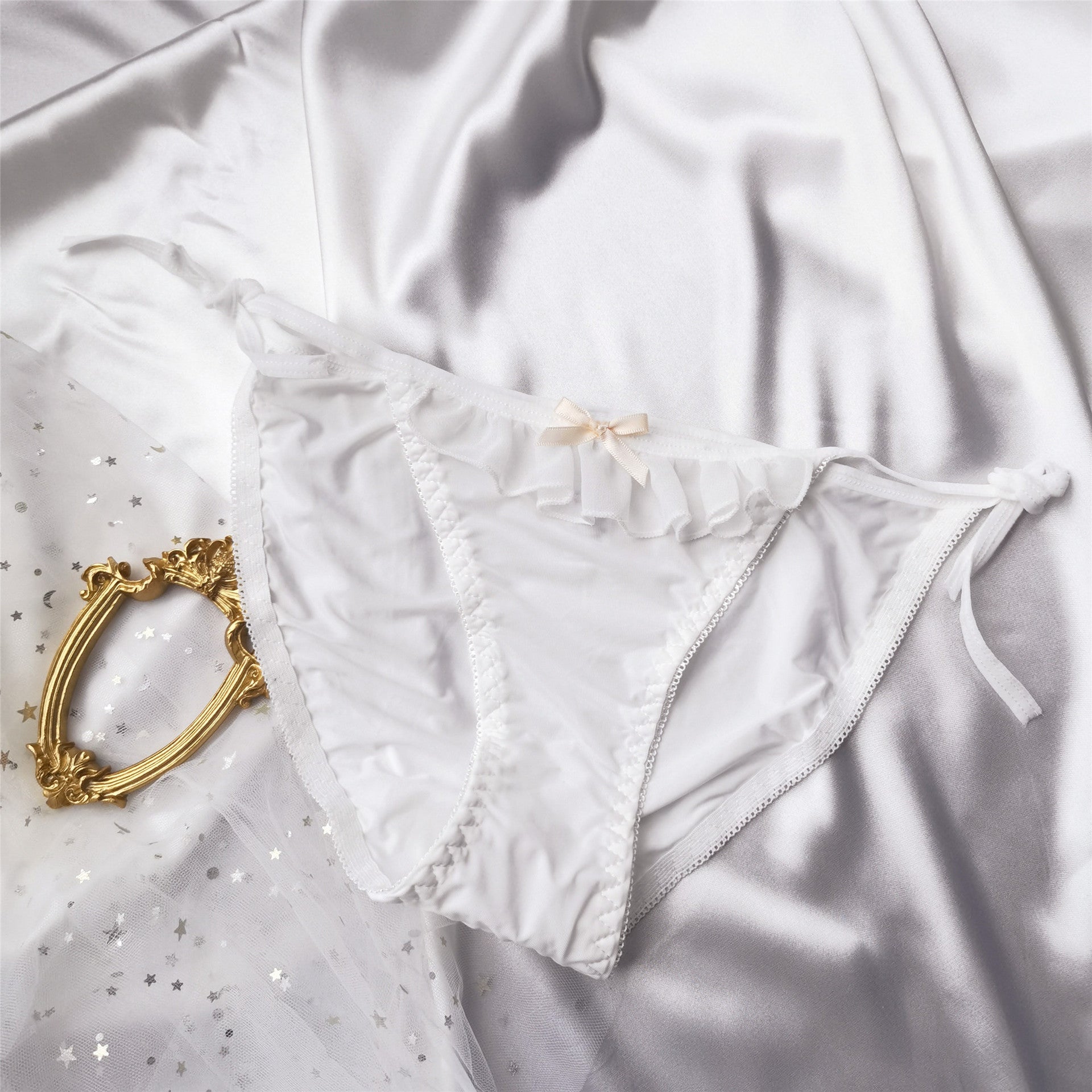 Flat lay of white Lolita maid lace-up panties with delicate ruffle trim and soft bow, displayed on satin – kawaii femboy underwear fashion