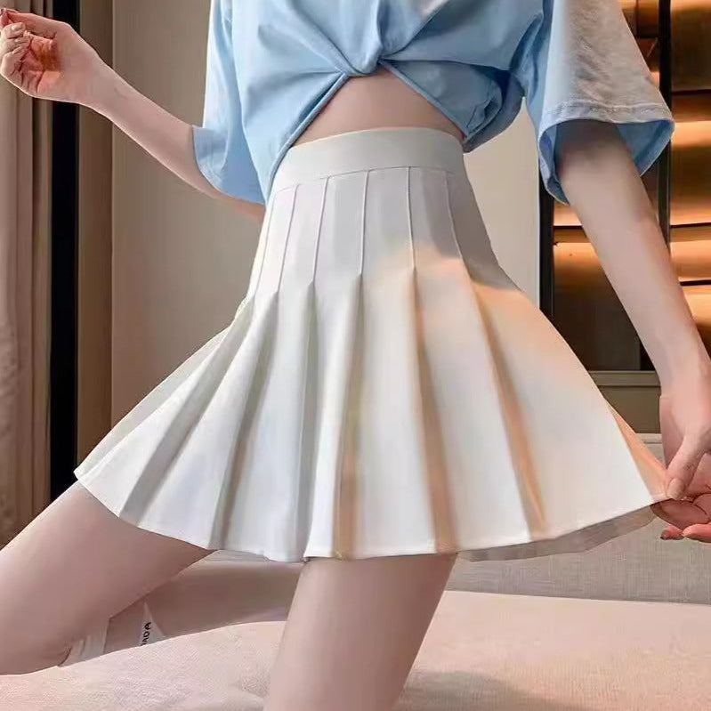 A white pleated skirt worn by a model paired with a light blue cropped shirt, set against a neutral, warmly lit indoor background. The clean pleats of the skirt add a sophisticated touch, making it a perfect piece for elegant femboy outfits and fashionable femboy clothing.