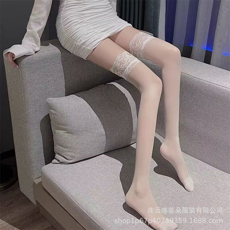 A model wearing white lace thigh-high stockings, sitting on a gray couch in an indoor setting. The delicate lace pattern brings a touch of femininity to any femboy fashion look, ideal for pairing with skirts or dresses for elegant femboy outfits.