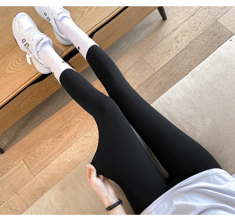 Overhead shot of black High Waist Yoga Leggings stretched for flexibility, paired with white sneakers and long socks. Captured indoors on a wooden floor, perfect for showcasing femboy clothing and activewear style.