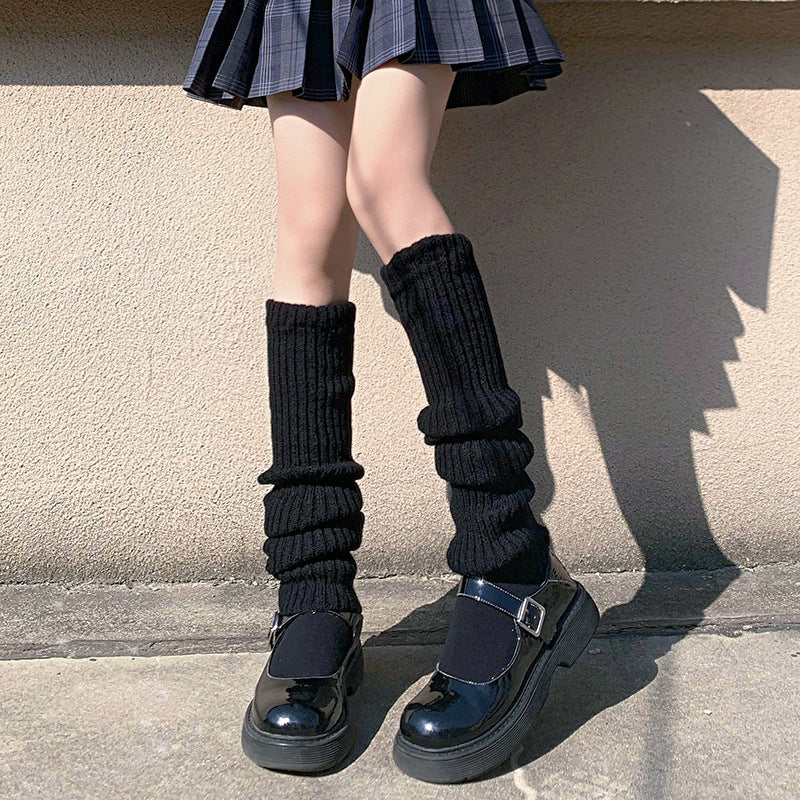 Black knitted leg warmers styled with glossy platform shoes and pleated skirt, front-facing lower-body shot, soft lighting, minimalist background, cozy femboy fashion aesthetic.