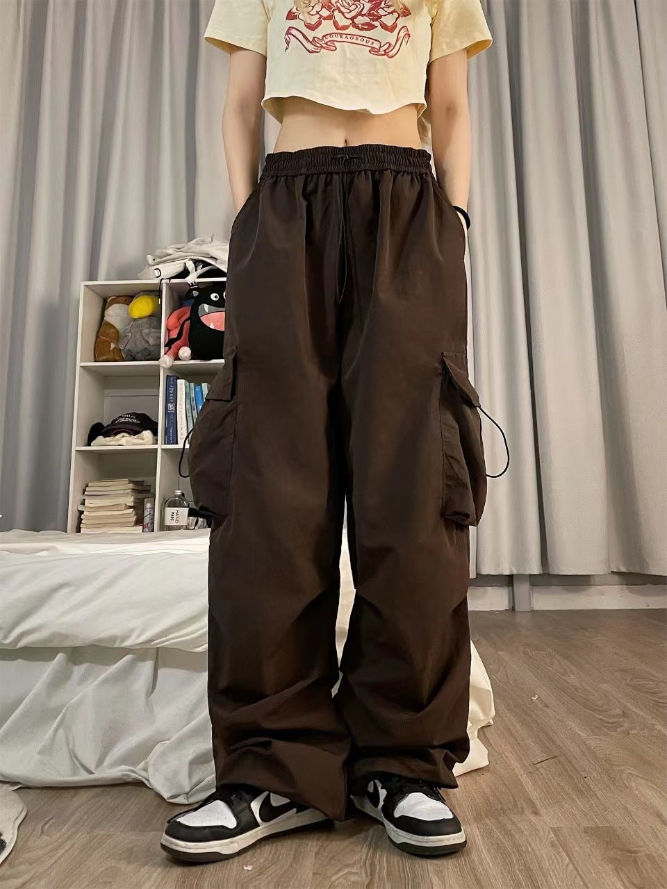 Indoor close-up of chocolate brown cargo pants with elastic waistband and deep side pockets, styled with a casual crop tee, showcasing relaxed fit – gender-neutral fashion, femboy clothing trends, stylish pants.