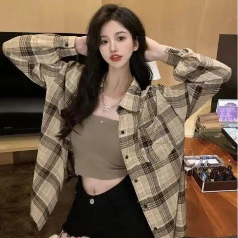 Medium shot of a person wearing a brown plaid button-up shirt over a cropped tank top. The person is posing indoors, hands behind their head, highlighting the oversized fit of the plaid shirt and its versatile style. Ideal for femboy fashion looks, with casual comfort and flair.