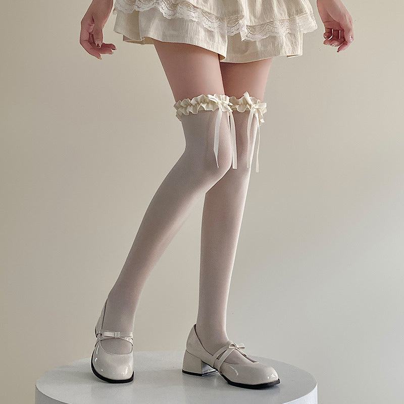 Close-up shot of cream-coloured Bowknot Lolita Thigh Highs styled with lace trim and bow details, paired with cream Mary Jane shoes. Taken in a neutral studio setting, showcasing femboy clothing and femboy fashion.