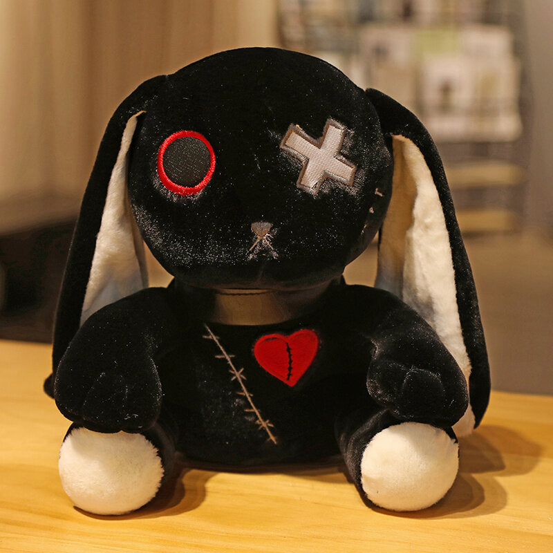 Black Dark Bunny plushie photographed front-on on a wooden tabletop, close-up product shot highlighting red stitched heart, cross eye embroidery, floppy ears with white inner lining, soft gothic bunny plush with moody aesthetic and plush texture.