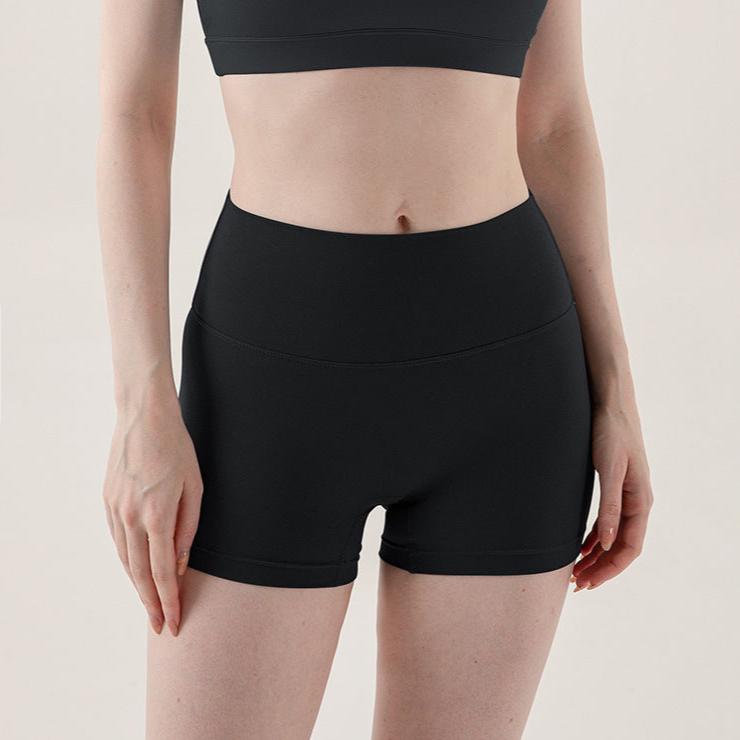 Front view of dark gray yoga shorts on a model, showcasing a high-rise waist and tight fit that highlights the figure. The image is framed from mid-waist to mid-thigh, set against a minimalist background.