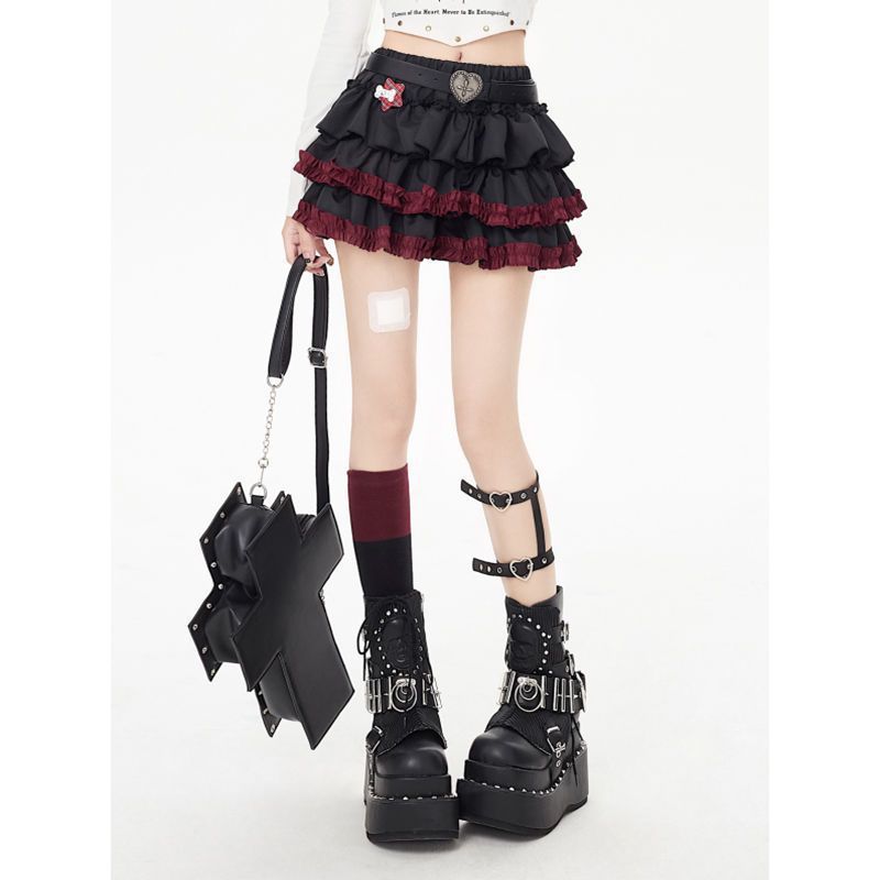 Model wearing a dark punk tiered femboy skirt with black and red ruffled layers, styled with platform boots and accessories, showcasing edgy gothic femboy outfit aesthetics.
