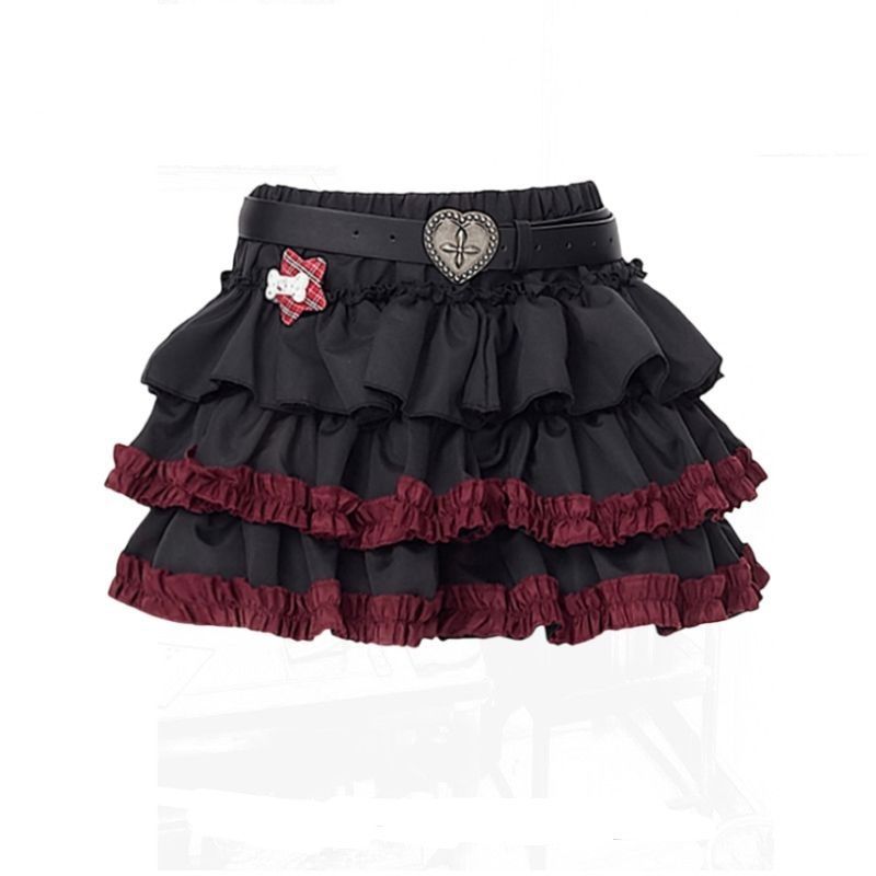 Product-only image of a dark punk tiered femboy skirt with black layered ruffles, deep red frill trim, and a heart-buckle belt detail, photographed on a white background for femboy fashion styling.