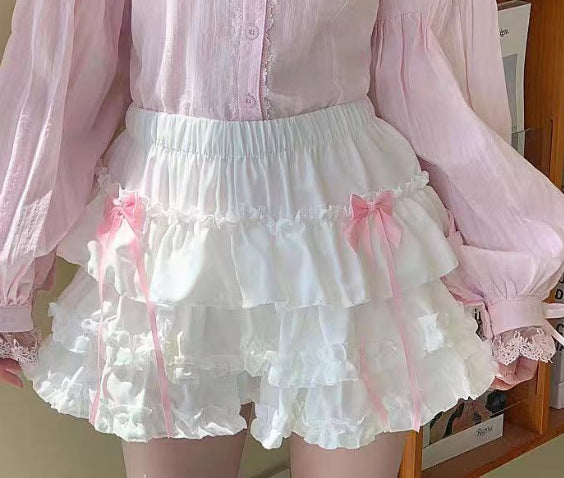 White tiered femboy skirt with pink ribbon bows and layered ruffles, front-facing mid-shot worn with sheer blouse, showcasing cute punk-lolita femboy fashion and feminine femboy clothing details.