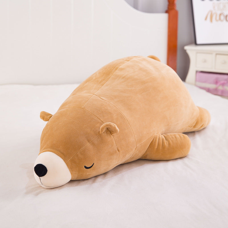 Wide lifestyle product shot of the Femboy Bear Plushie resting on a bed, photographed from a slightly elevated front-left angle with soft indoor lighting, featuring a warm brown and cream color palette and smooth plush texture, a cozy bedroom accessory from a femboy clothing store that complements cute femboy outfit aesthetics.
