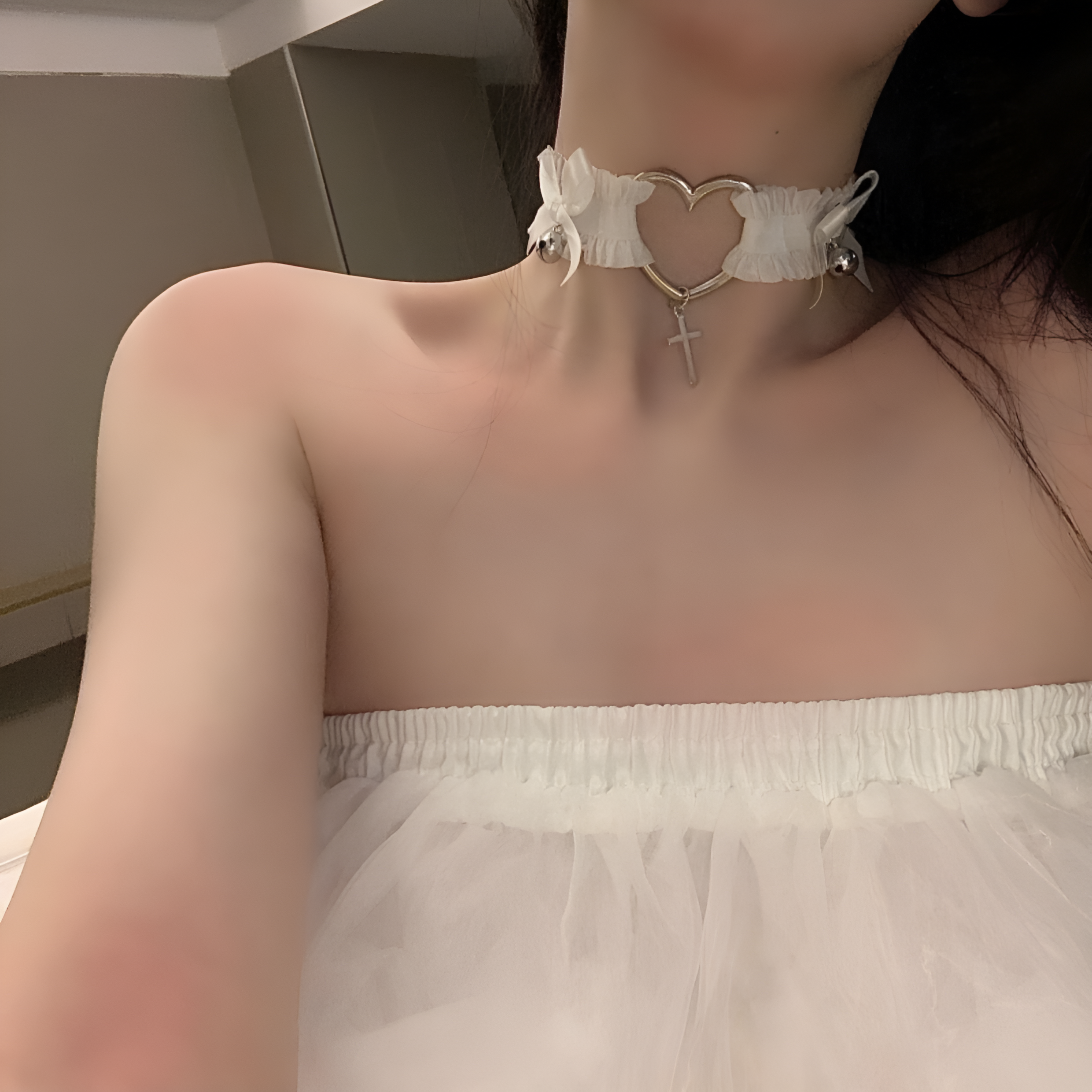 Close-up of the white Femboy Cross and Heart Choker, showcasing the heart-shaped metal design with a dangling cross. The white ribbon bows and silver bells enhance the cute and elegant femboy style, ideal for femboy fashion and femboy clothing.
