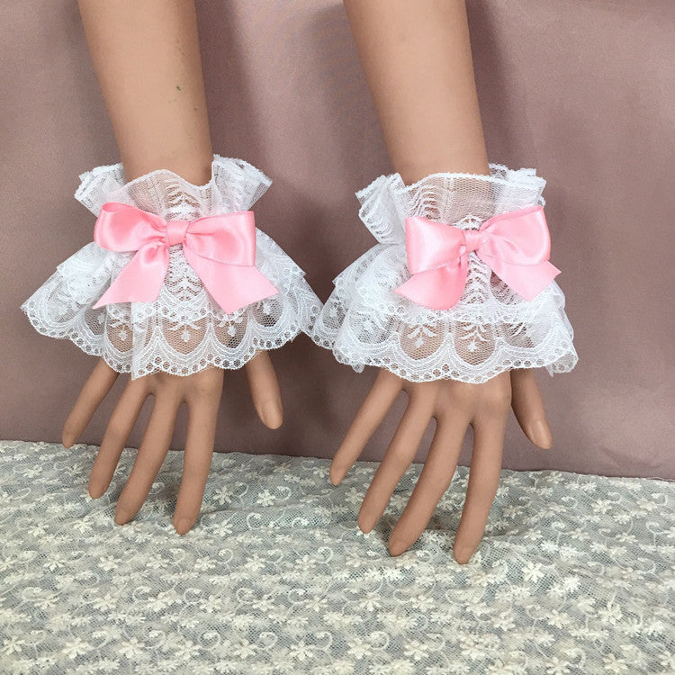 A pair of white lace bracelets adorned with pastel pink bows, elegantly arranged on mannequin hands against a soft pink background. The delicate lace and playful bows make these accessories perfect for enhancing femboy outfits or femboy fashion looks.