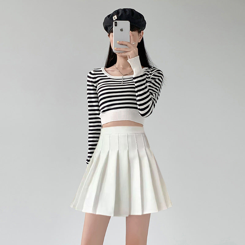 Full-body shot of a model wearing a white pleated skirt with a striped crop top and beret, captured in a mirror selfie. The clean lines of the pleated skirt and casual styling showcase an excellent example of femboy clothing. The overall outfit embodies casual but stylish femboy fashion, making it perfect for femboy outfits.