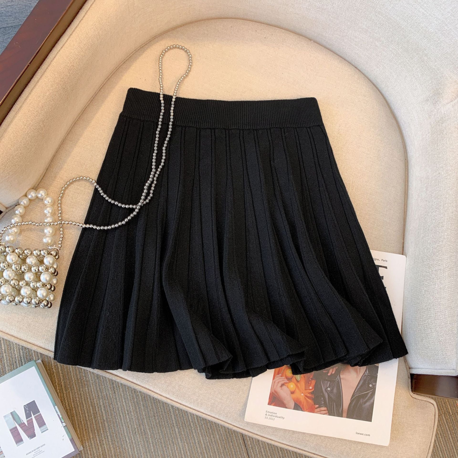 Close-up of a black pleated skirt displayed on a cream-colored chair. The high-waisted design and chic pleats make this a trendy option for femboy outfits and an essential piece of femboy clothing. Perfect for those embracing femboy fashion. Keywords: femboy clothing, femboy outfits, femboy fashion.