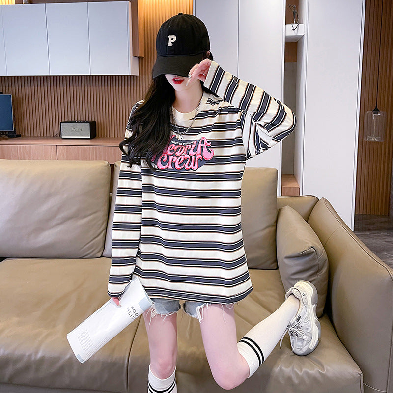 A front view of a model lounging on a couch, wearing a long sleeve striped sweatshirt in black and white, styled with a casual black baseball cap and denim shorts. Ideal for layering in femboy fashion looks.