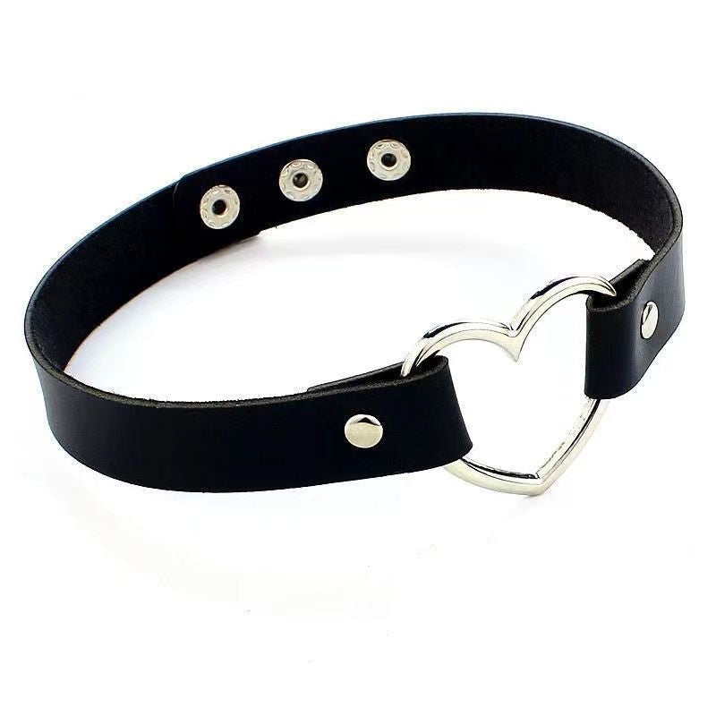 Black leather gothic choker with silver heart-shaped metal ring centerpiece, adjustable strap and snap-button closure, minimalist femboy fashion accessory photographed on white background, close-up product shot.