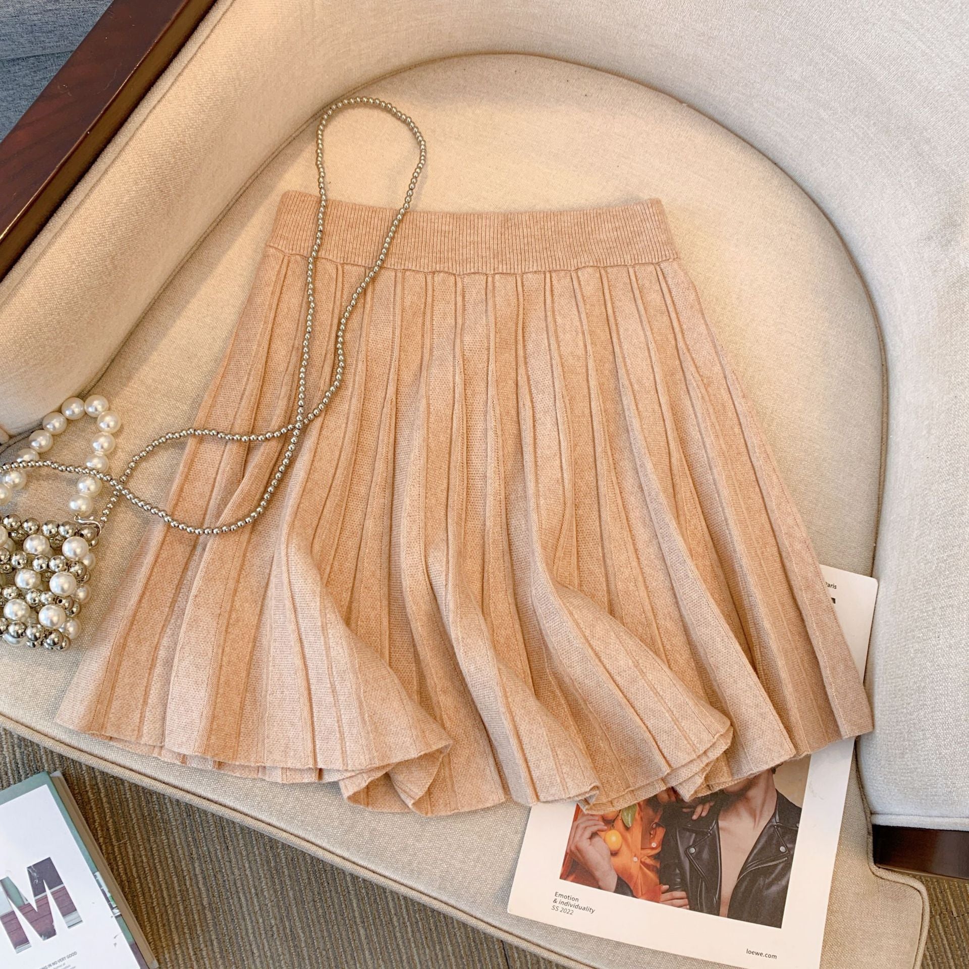 Close-up of a beige pleated skirt placed on a cream-colored chair. The high-waist design and elegant pleats are ideal for completing femboy outfits, making this piece a stylish addition to any femboy clothing collection. Keywords: femboy clothing, femboy outfits, femboy fashion.