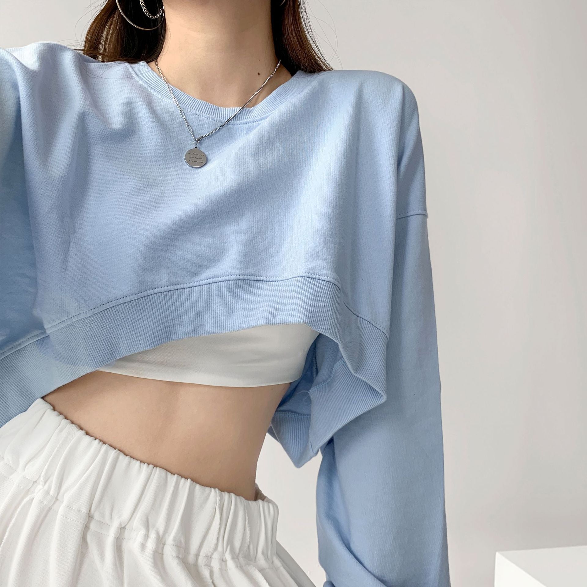 Light blue cropped long sleeve sweatshirt styled with a white skirt, showcasing a trendy femboy outfit, with a clean, minimalist background.