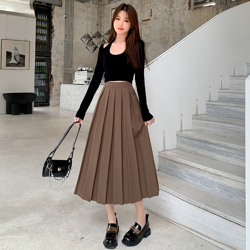 Full-body shot of model in a brown high-waisted pleated skirt with a black crop top and chunky loafers, taken in a stylish, industrial-themed setting. An ideal femboy style look for a chic and bold aesthetic.