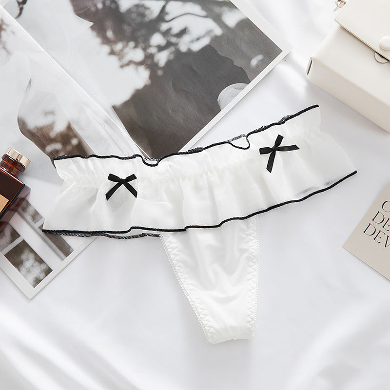 Top-down flatlay shot of white ruffled femboy maid panties trimmed with black bows, displayed on a bright white background for a clean femboy lingerie aesthetic.