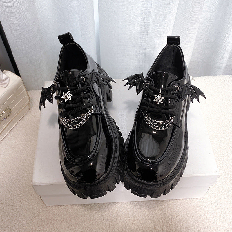 Front view of Gothic Lolita School Pumps featuring a glossy black finish with winged accents and decorative chains, showcasing a unique star pendant on the laces. Ideal for femboy fashion with a dark, elegant twist.