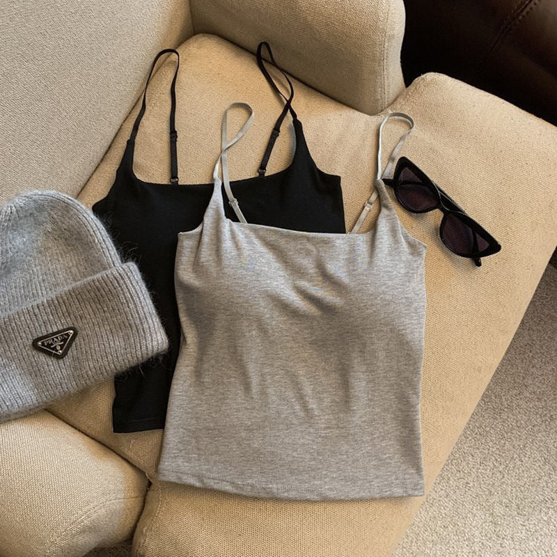 A gray camisole placed next to a black camisole on a beige couch, alongside a gray designer beanie and black sunglasses. The simple and chic design complements femboy outfits and solid colour fashion.