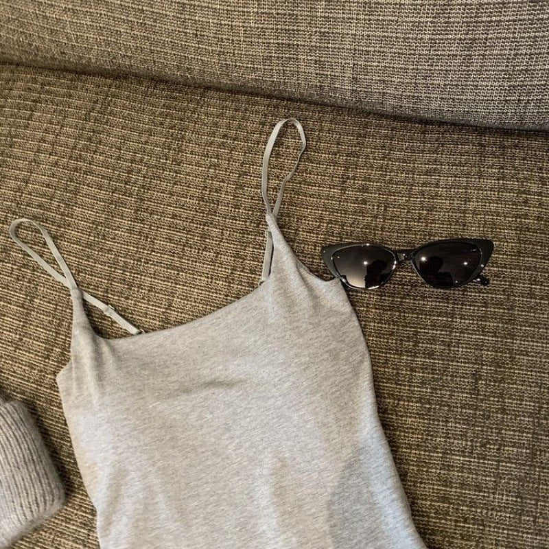 A gray solid colour camisole, displayed on a brown couch next to black sunglasses. This versatile camisole is perfect for casual femboy fashion looks and femboy outfits.