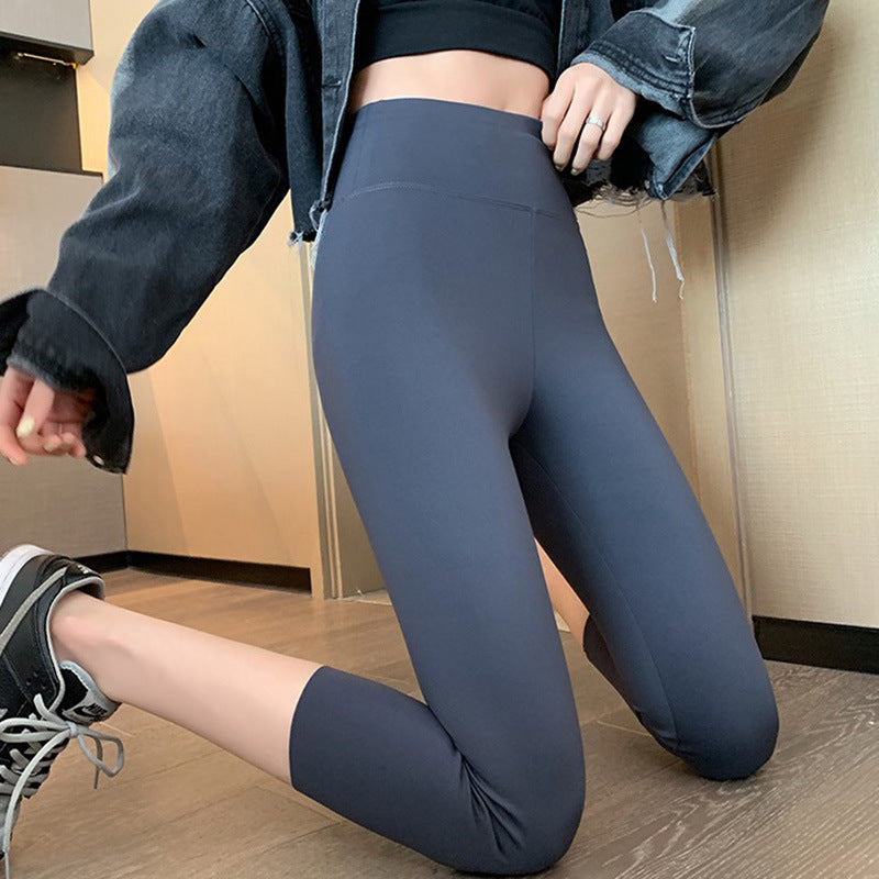 Side view of gray High Waist Yoga Leggings in capris length, paired with a black sports bra and denim jacket. Captured indoors on a sleek wooden floor, highlighting femboy clothes and workout fashion.