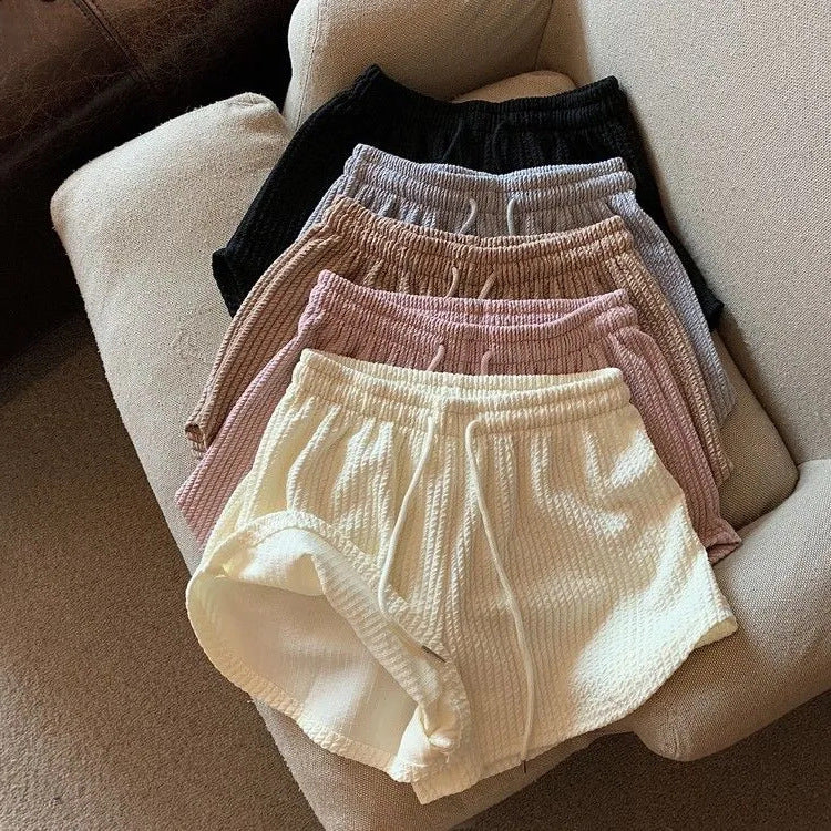 Flat-lay of assorted colours of high-waist yoga shorts on a beige couch, showcasing the vibrant options for femboy clothing and outfits.