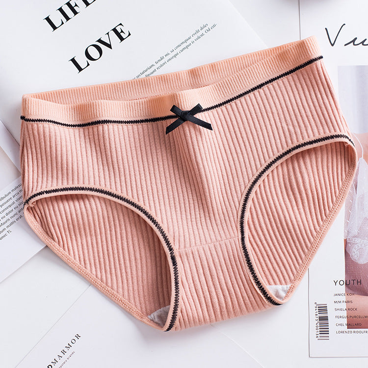 overhead shot of a peach ribbed brief with black contrast trim and delicate lace edging on a clean white surface, perfect for femboy lingerie styling.