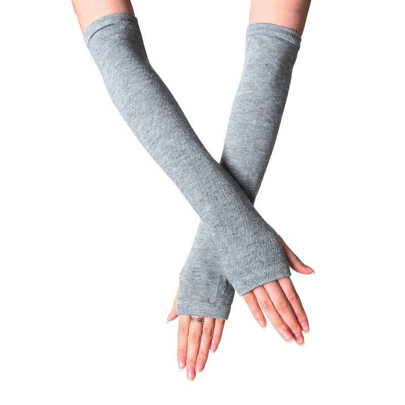 Close-up of hands wearing light grey fingerless knit arm warmers, long and soft, covering arms with a cozy fit. Ideal for femboy clothing and femboy outfits to keep warm in winter fashion.