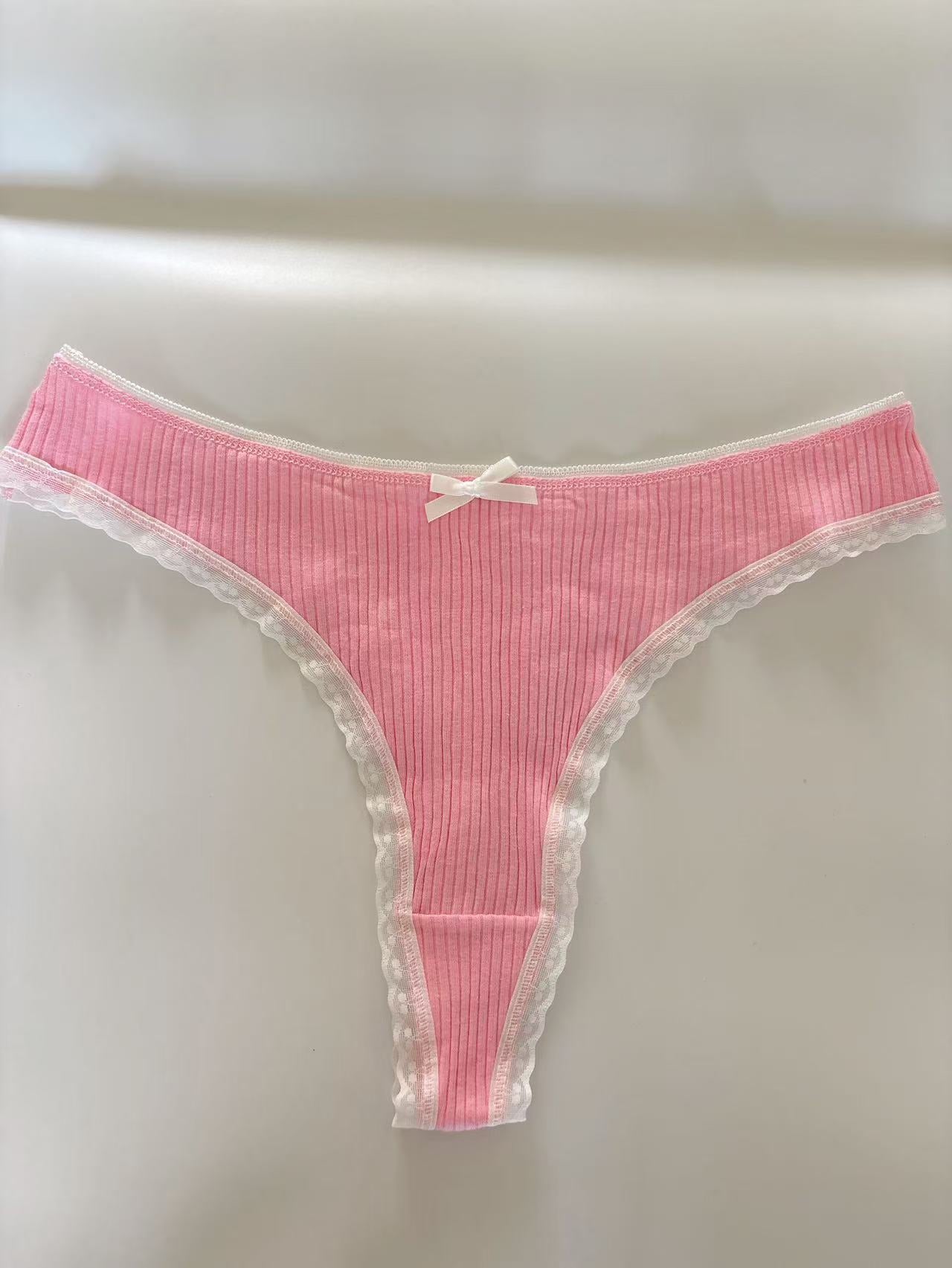 Flat-lay of a pink Bowknot Lace Trim Thong with ribbed texture, white lace detailing, and a bowknot embellishment. Captured on a soft white surface to emphasize elegant femboy fashion.